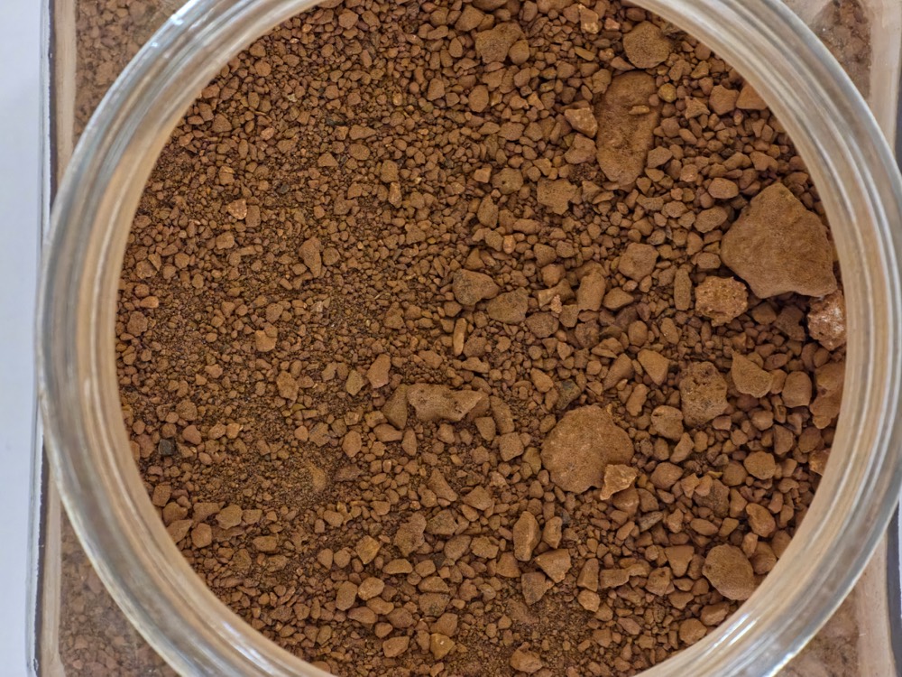 Red mud waste sample: reddish-brown granular bauxite residue in a jar